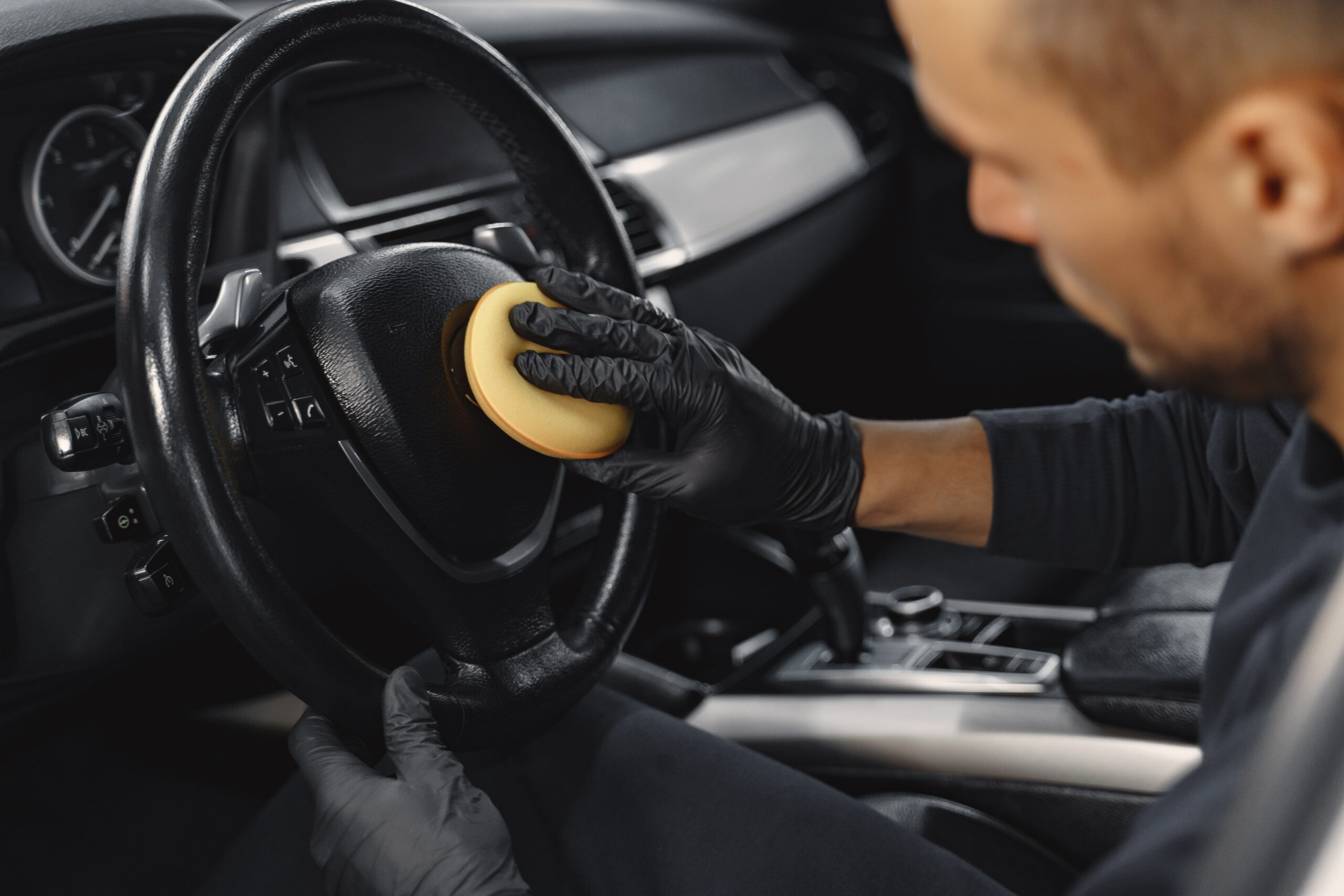 Man in a garage. Worker polish inside a car. Man in a black uniform.